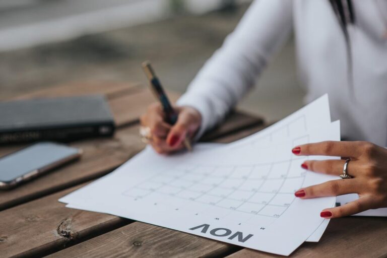 Woman writing notes on paper while looking at a calendar